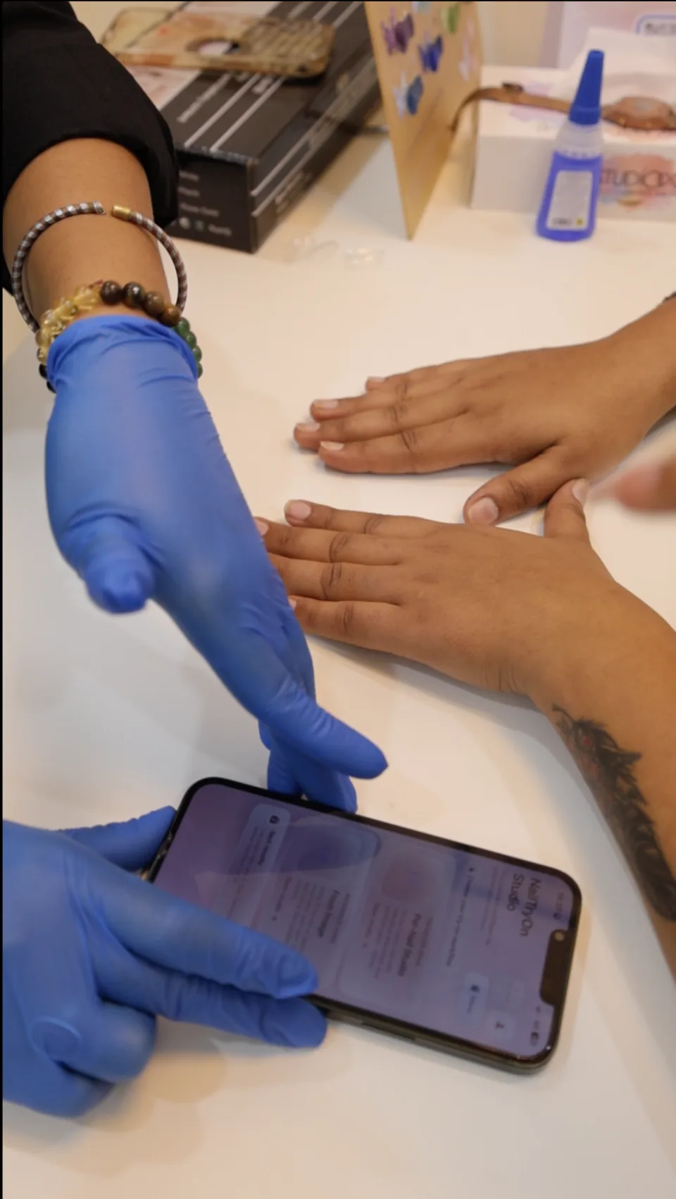 A nail technician positions a phone beside the client’s hand at the consultation table.