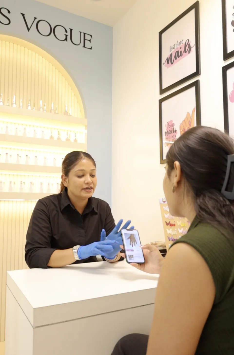 A nail technician and client discuss a virtual nail preview on a phone at Studio99’s Nails Vogue nail station.