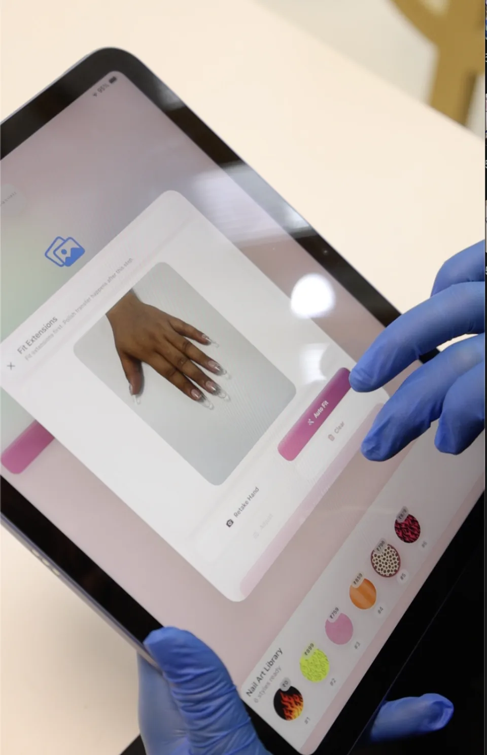 A technician adjusts a nail design on the client’s hand in the iPad editor.